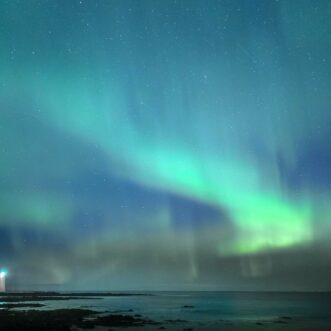 Nordlicht bei Reykjavik mit Leuchtturm und Sternenhimmel.