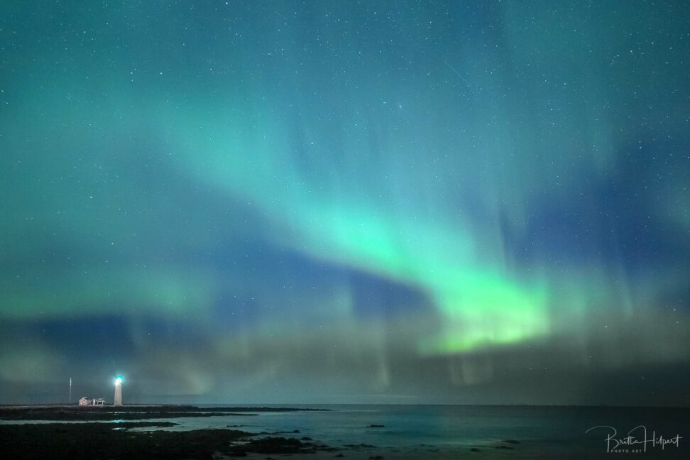 Nordlicht bei Reykjavik mit Leuchtturm und Sternenhimmel.