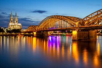 Kölner Dom mit Hohenzollernbrücke, beleuchtet,und Spiegelung im Rhein.