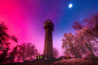 Polarlicht über dem Köppelturm und der Köppelhütte im Westerwald in Magentafarbenen Licht, das vom Raureif auf den Bäumen widergespiegelt wird.